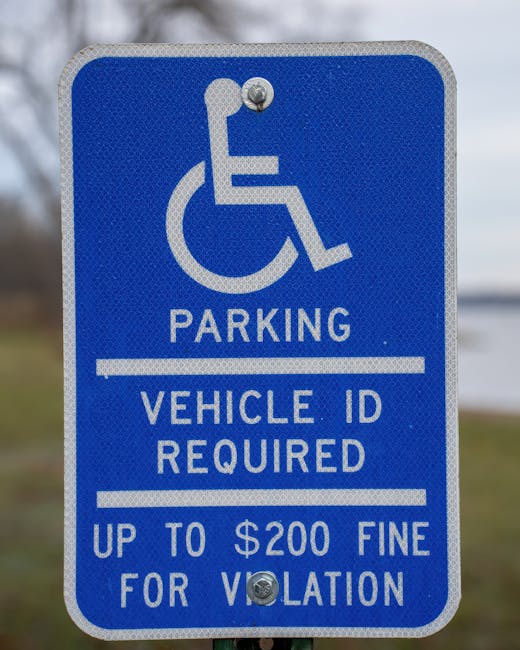 A close-up view of a blue parking sign featuring a white wheelchair symbol indicating accessible parking. The sign displays the words 'PARKING', 'VEHICLE I.D REQUIRED', and 'UP TO $200 FINE FOR VIOLATION' in white capital letters, with horizontal white lines separating each section. The sign is mounted on a metal pole with a visible bolt at the top and bottom, set against an overcast sky and a distant blurred background. The image is relevant to house removals and moving services by highlighting parking regulations that may affect loading and unloading during a home relocation in Raynes Park. The image is clear, well-lit, and demonstrates the importance of understanding local parking restrictions enforced by authorities, which Man with Van Raynes Park carefully considers during the logistics of furniture transport and packing and moving processes.
